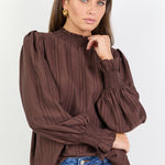 Woman wearing a brown blouse with puffed sleeves and blue jeans on a white background