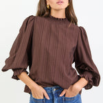 Woman wearing a brown blouse with puffed sleeves and blue jeans on a white background