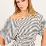 A woman modeling a black and white horizontally striped off-the-shoulder top with wide short sleeves, set against a plain light beige background.