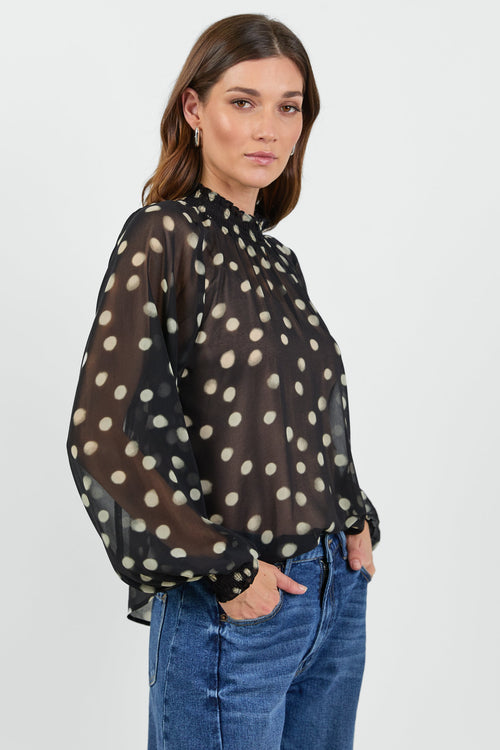 Woman wearing a black blouse with white polka dots and blue jeans on a white background