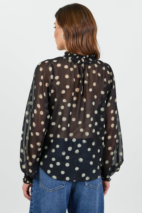 Woman wearing a black polka dot blouse and blue jeans on a white background