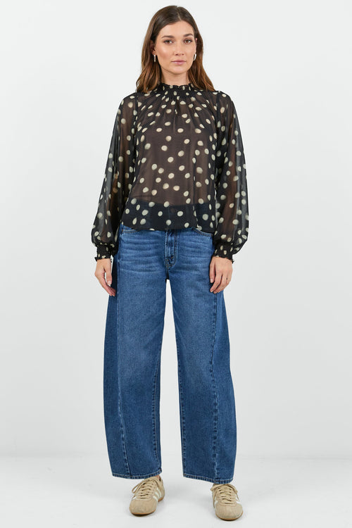 Woman wearing a sheer black polka dot blouse and blue jeans on a white background
