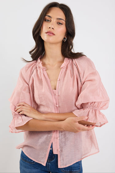 Woman wearing a pink blouse with ruffled sleeves on a white background
