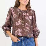Woman wearing a floral blouse with long sleeves and blue jeans on a white background