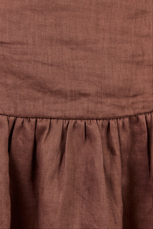 Close-up of a brown textured fabric garment, showing a gathered waist seam and linen-like texture.