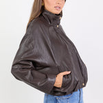 Woman wearing a brown leather jacket and blue jeans on a white background