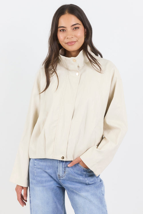Woman wearing a cream jacket and light blue jeans on a white background