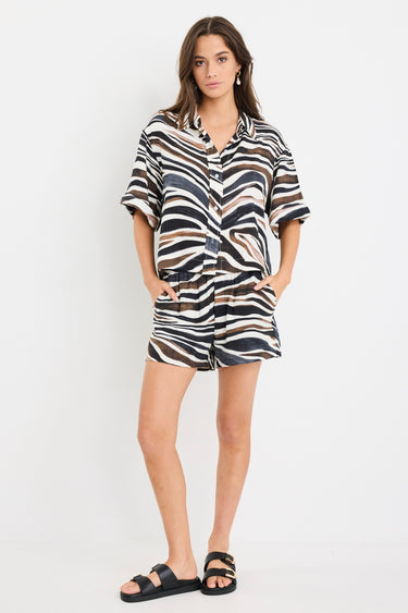 Woman wearing mid-rise chocolate zebra print shorts with an elastic waistband, styled casually with a black top and black sandals.