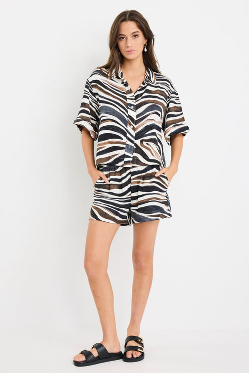 Woman wearing mid-rise chocolate zebra print shorts with an elastic waistband, styled casually with a black top and black sandals.