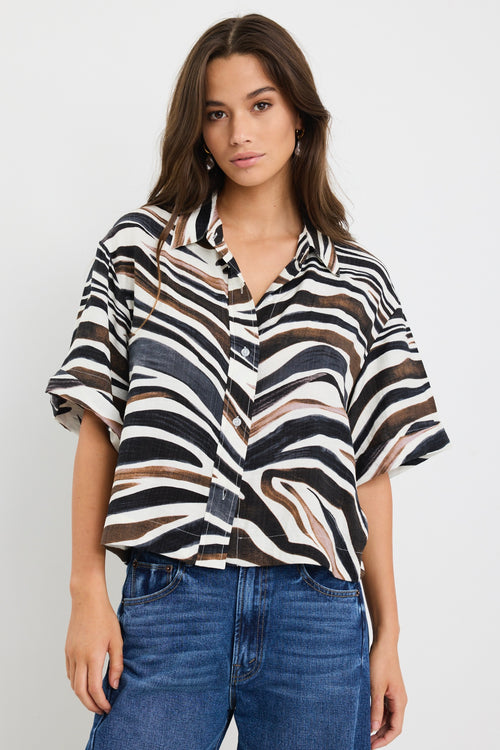 Woman wearing a relaxed-fit short sleeve zebra print shirt in chocolate, black, and white tones, styled with high-rise blue jeans.