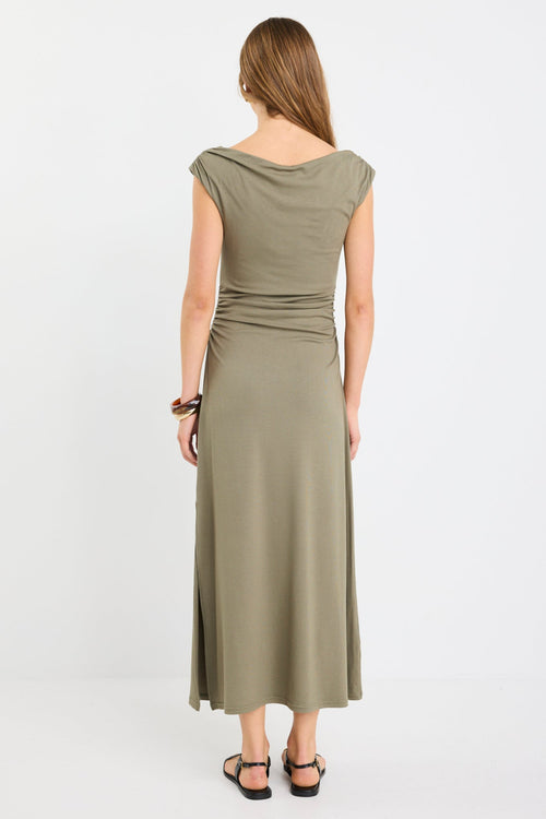 Woman wearing a sleeveless khaki midi dress with boat neckline and ruched side detailing, styled with black strappy sandals.