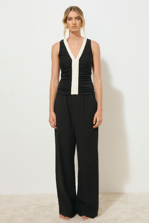 Black sleeveless tank top with contrast cream band detail down the centre front and neckline, featuring a ruched bodice and low V-neckline, worn by a model sitting against a neutral background.