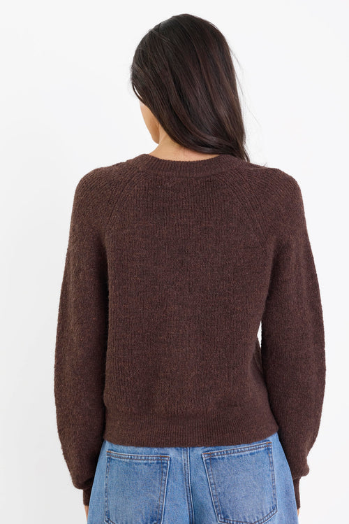Person wearing a brown sweater and blue jeans on a white background