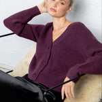 Woman wearing a purple cardigan sitting on a white bench.