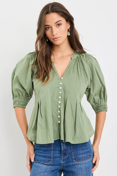 Woman wearing a moss green short sleeve button-front top with puff sleeves, pleated detail, and flared hem, styled with high-waist blue jeans.
