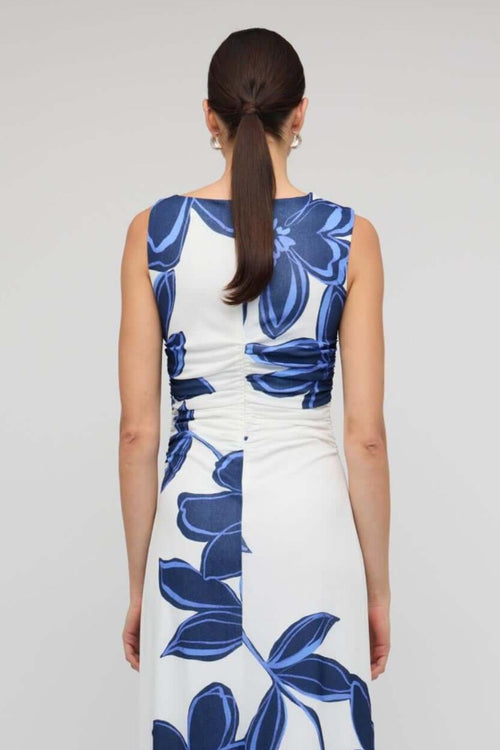 Woman wearing a sleeveless white midi dress with large blue floral print, featuring a side cutout detail and slim fit through the waist.