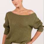 A woman wearing an olive green off-the-shoulder knit sweater and cream drawstring pants, photographed against a clean off-white studio background.
