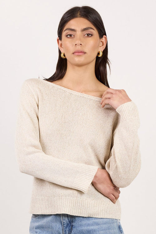 A woman modeling a cream-colored knit sweater and light-wash denim shorts against a plain white studio background.