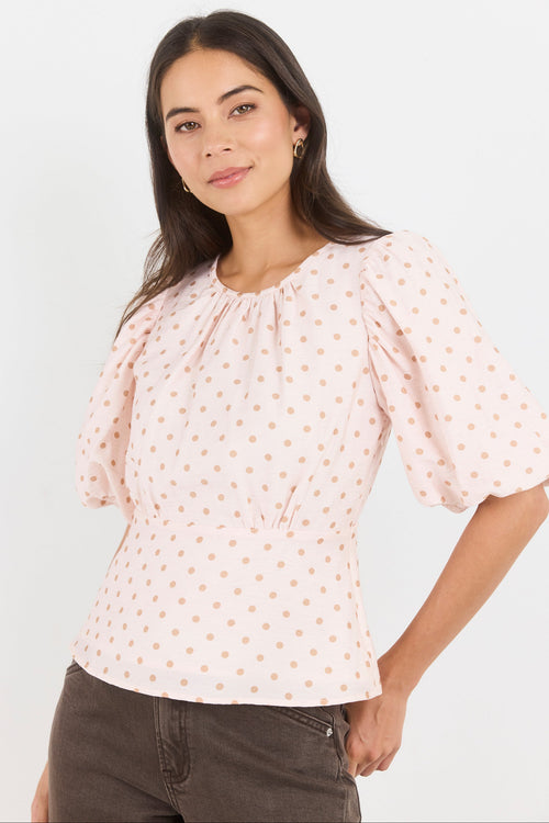 Woman wearing a light pink blouse with puff sleeves against a white background