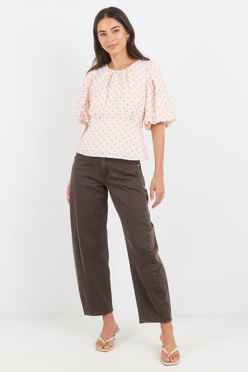 Woman wearing a patterned blouse and brown pants on a white background