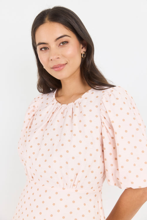 Woman wearing a light pink blouse with subtle polka dot pattern on a white background