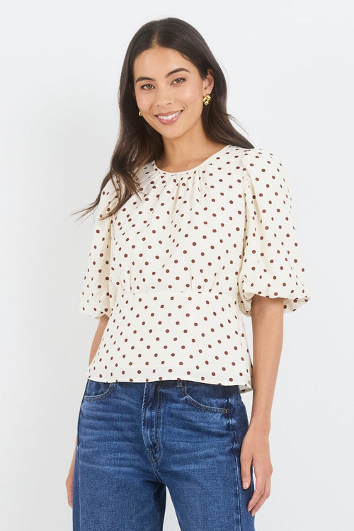 Woman wearing a polka dot top and blue jeans on a white background