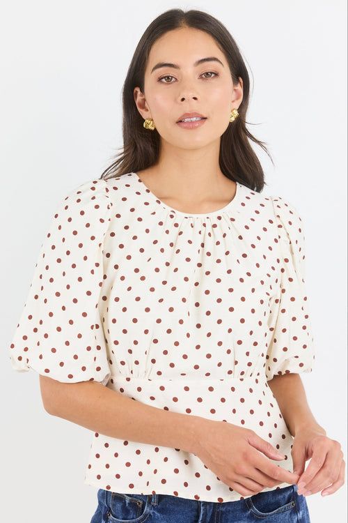 Woman wearing a white blouse with red polka dots and blue jeans on a light gray background