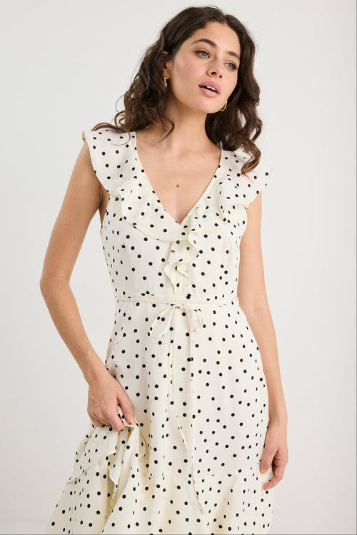 Woman wearing a white dress with black polka dots against a plain background
