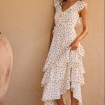 Woman in a white polka dot dress standing next to a large pot against a beige wall.