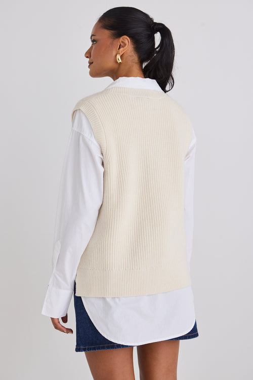 Model wears a knit vest with a white shirt 