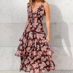 Woman wearing a floral dress standing against a light gray wall.