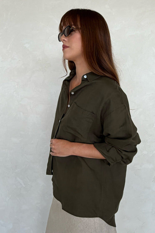 Woman wearing an olive green shirt against a white wall