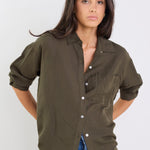 Woman wearing an olive green shirt and blue jeans against a white background