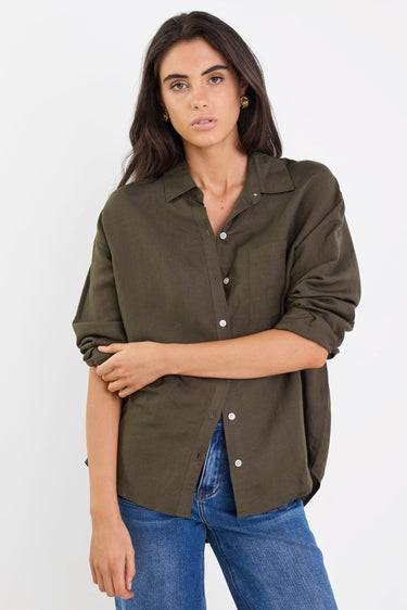 Woman wearing an olive green button-up shirt and blue jeans on a white background