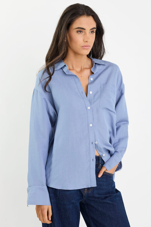 Woman wearing a light blue button-up shirt and dark jeans on a white background