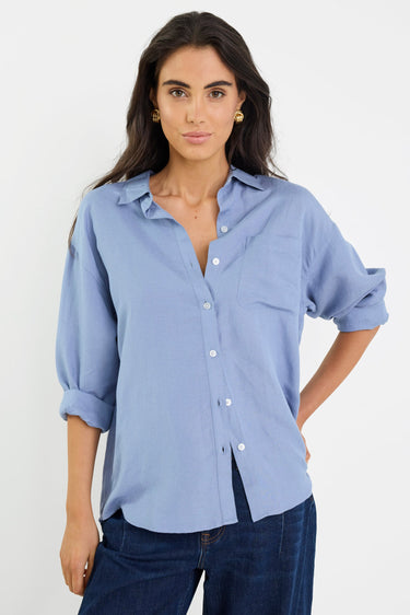 Woman wearing a light blue button-up shirt and dark blue jeans against a white background