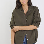 Woman wearing an olive green shirt and blue jeans against a white background