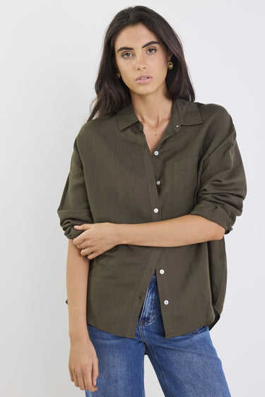 Woman wearing an olive green shirt and blue jeans against a white background