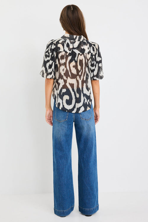 Woman wearing a black and cream zebra print short sleeve shirt with puff sleeves, button front, and tie waist detail, styled with blue jeans.