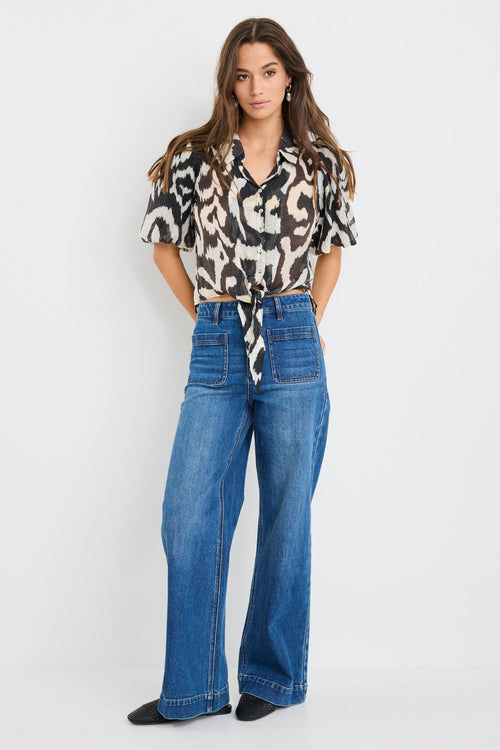 Woman wearing a black and cream zebra print short sleeve shirt with puff sleeves, button front, and tie waist detail, styled with blue jeans.