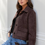 Woman wearing a brown jacket and blue jeans against a white wall