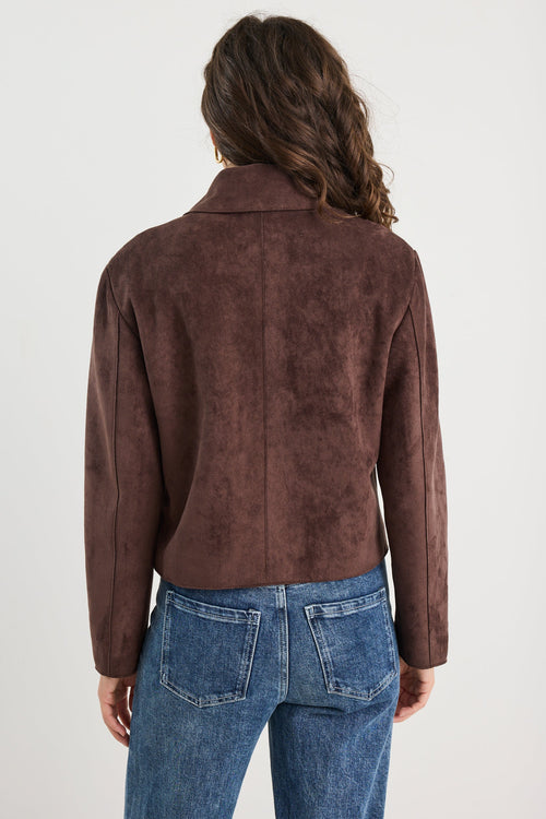 Person wearing a brown suede jacket and blue jeans on a white background