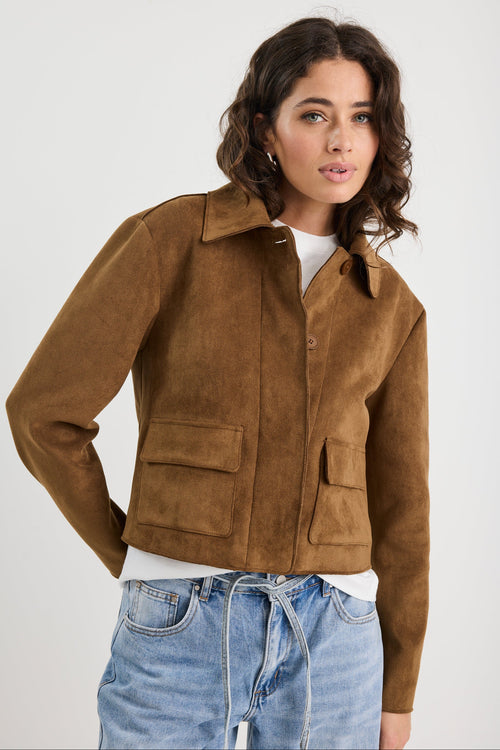 Woman wearing a brown suede jacket and blue jeans on a white background