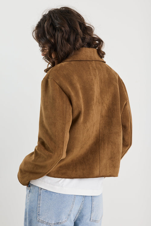 Person wearing a brown jacket and light blue jeans on a white background