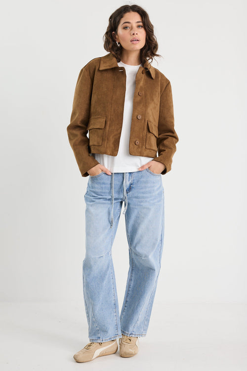 Woman wearing a brown jacket, white shirt, and light blue jeans on a white background