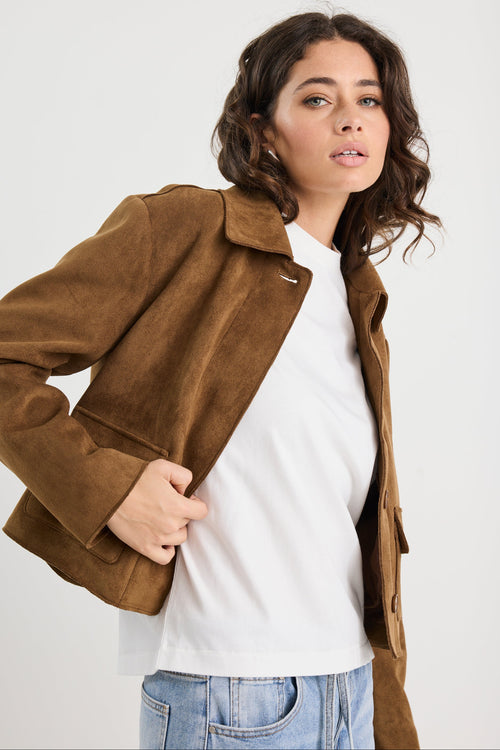 Woman wearing a brown jacket over a white shirt with a plain background