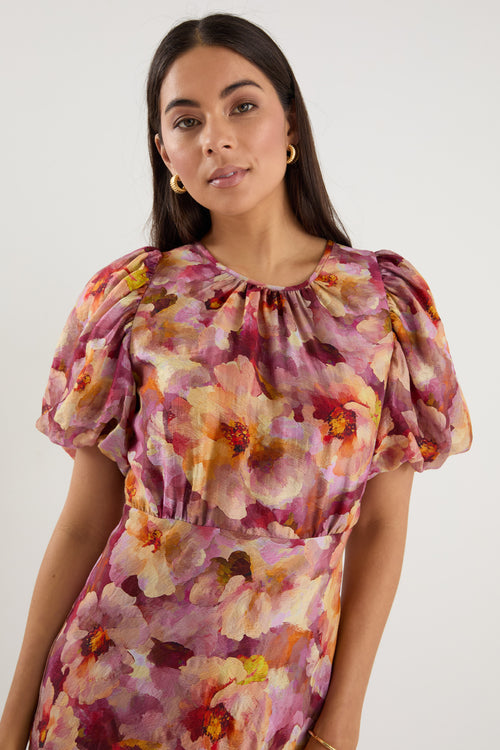 Woman wearing a pink and multi-tone floral midi dress with puff short sleeves, bias cut, and lined finish.