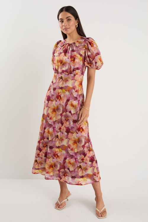 Woman wearing a pink and multi-tone floral midi dress with puff short sleeves, bias cut, and lined finish.