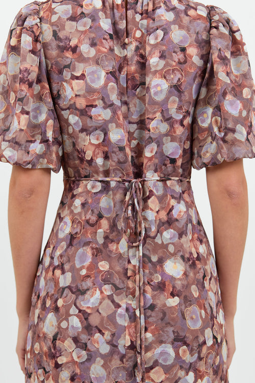 A woman wearing a floral midi dress in shades of lilac, blush, and soft pink, with puffed short sleeves and a relaxed fit.