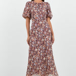 A woman wearing a floral midi dress in shades of lilac, blush, and soft pink, with puffed short sleeves and a relaxed fit.